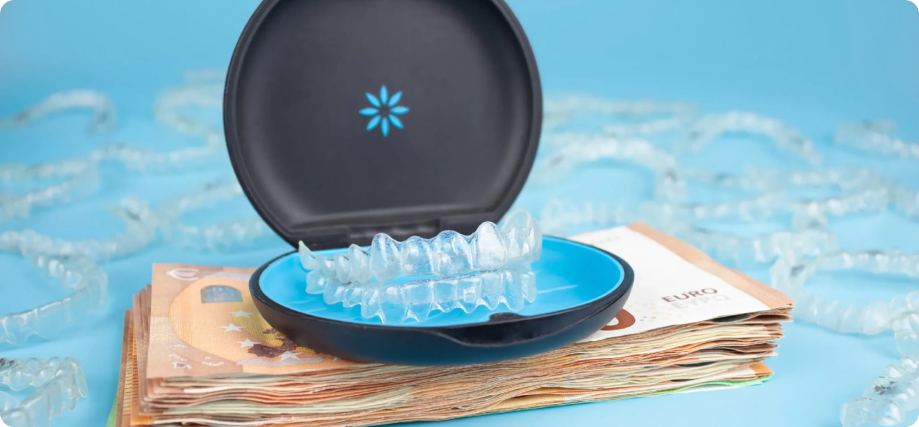 A dental aligner case is open, displaying clear aligners. It is placed on a stack of Euro banknotes with several aligners scattered in the background against a blue backdrop.