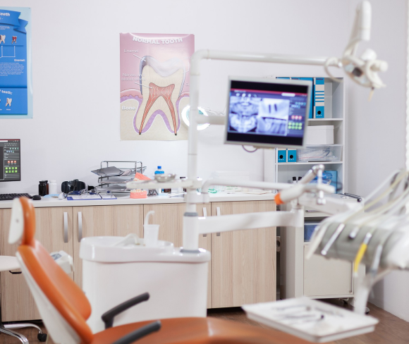 A dental office featuring an examination chair, dental equipment, a monitor and a tooth diagram on the wall.