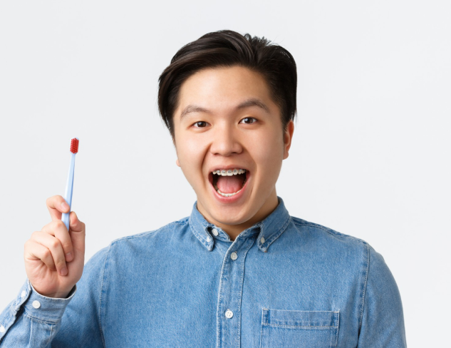 Person in a denim shirt holding a blue toothbrush, smiling with an open mouth against a plain background.