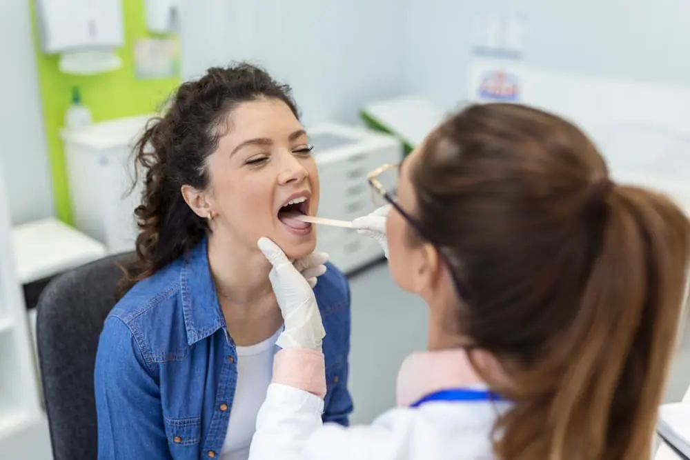A doctor examines a patient's throat using a tongue depressor in a medical office