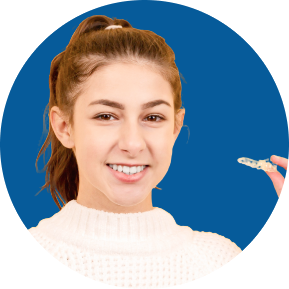 A person with long hair in a ponytail holds a clear dental aligner while smiling. The background is a solid blue.