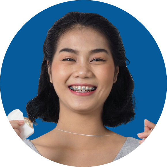 Person smiling with braces, holding dental floss against a blue background.