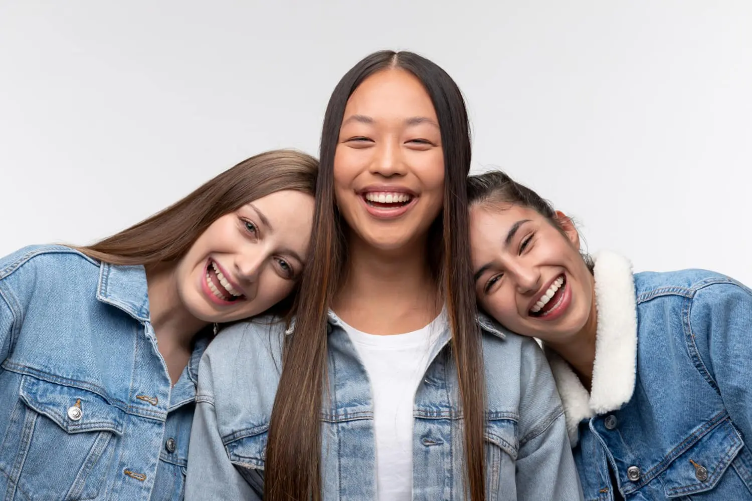 Three people, showcasing their best orthodontics with confident smiles, wear denim jackets as they pose against a plain background.