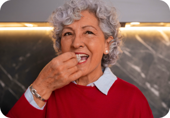 Elderly woman with curly gray hair in red sweater taking a pill.