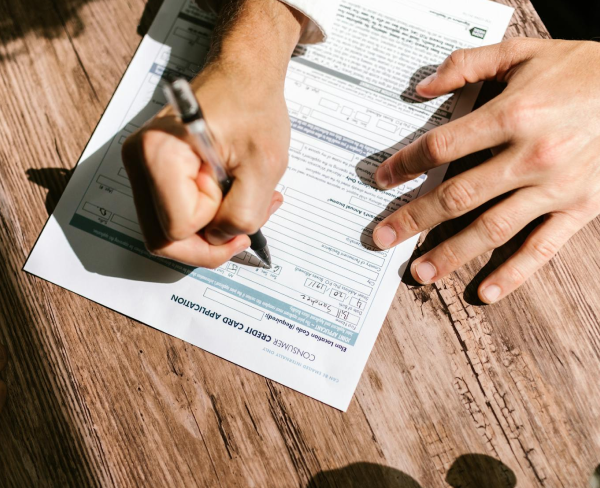 A person fills out a commercial credit card application form on a wooden table.