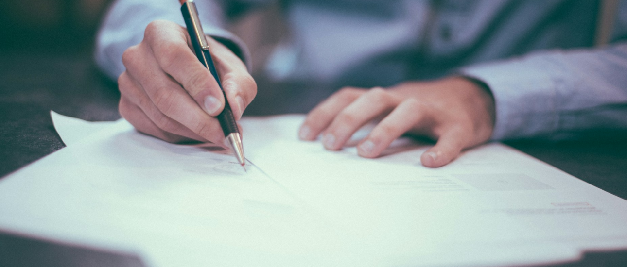 Person writing on a paper with a pen, wearing a long-sleeved shirt.