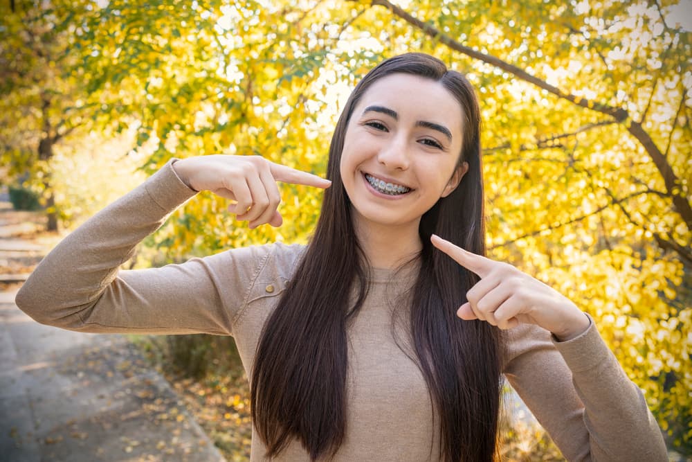 Teenager grinning with vibrant bands on their metal braces, proud of their orthodontic progress.