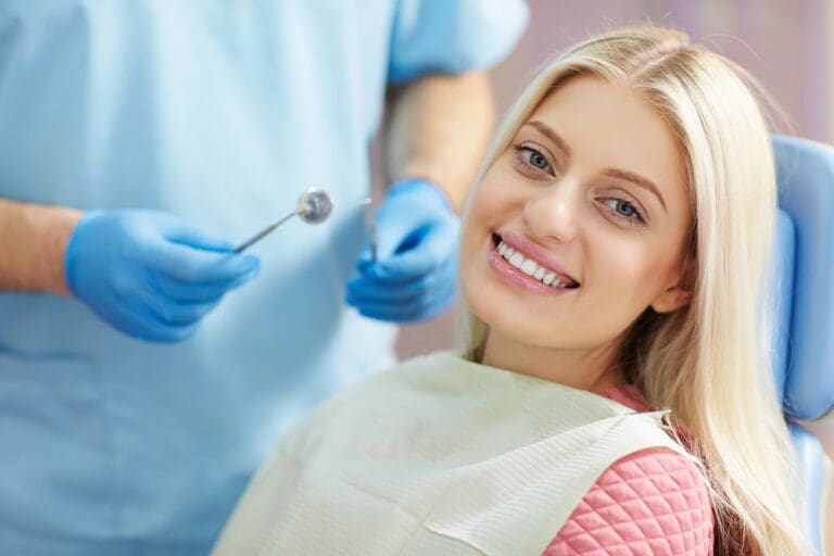 A woman in a dental chair smiles while a dentist holds a dental tool nearby.