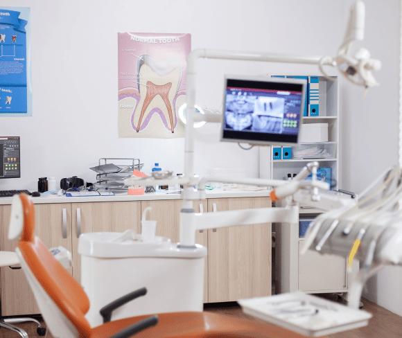 A dental office featuring an examination chair, dental equipment, a monitor and a tooth diagram on the wall.