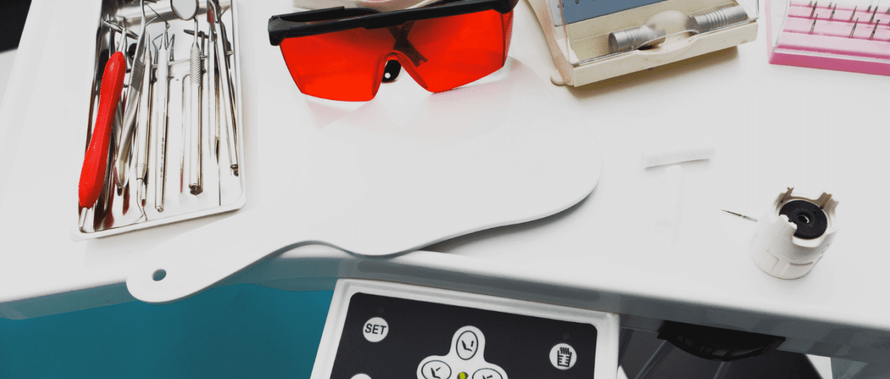 Dental tools, red protective glasses, a dental mirror and control panel on a white surface.