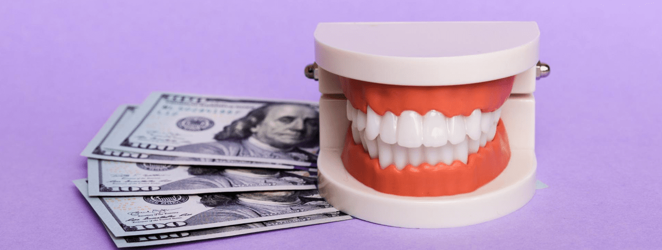 A set of artificial teeth is placed next to several US $100 bills on a purple background.