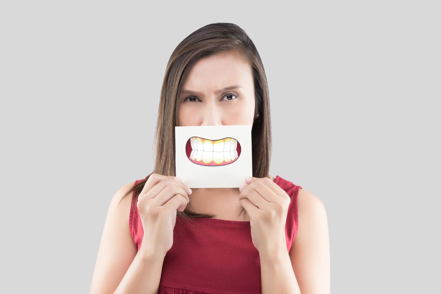 A woman in a red dress holds a paper with a large cartoon smile in front of her mouth, covering her actual expression In Austin, TX.