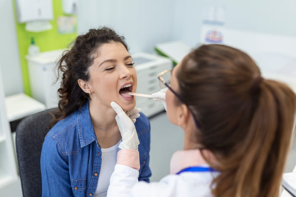 A doctor examines a patient's throat using a tongue depressor in a medical office