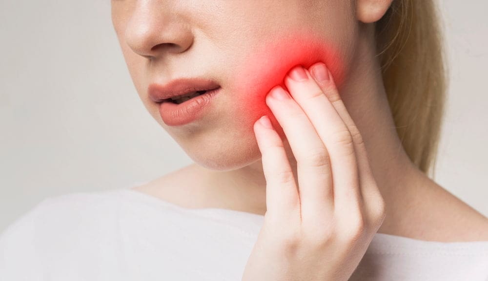 A person holds their cheek with a red area indicating facial pain or toothache