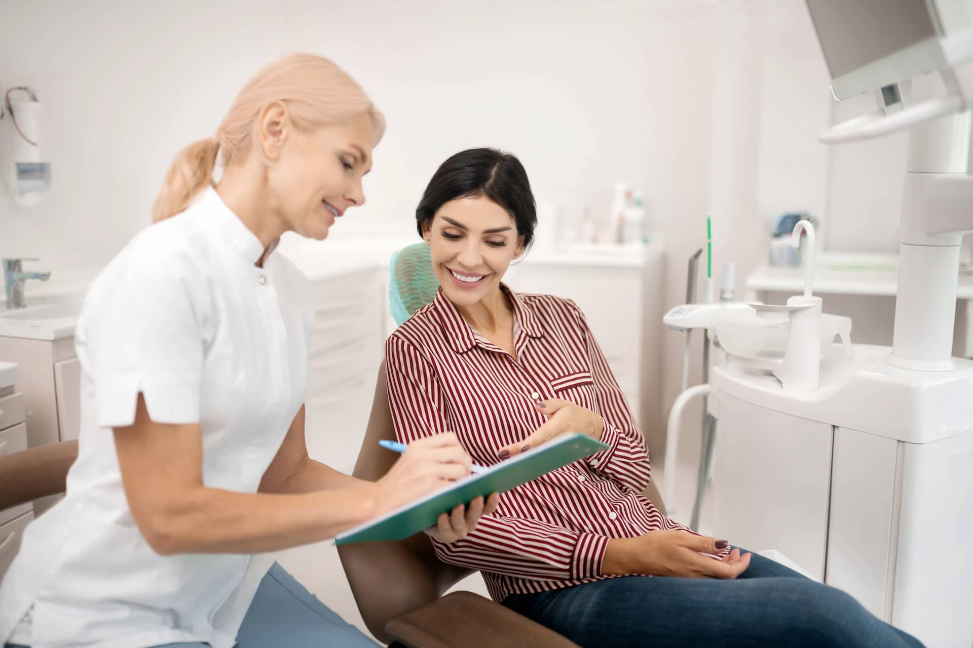 Dentist showing a clipboard to a patient seated in a dental chair, both smiling.