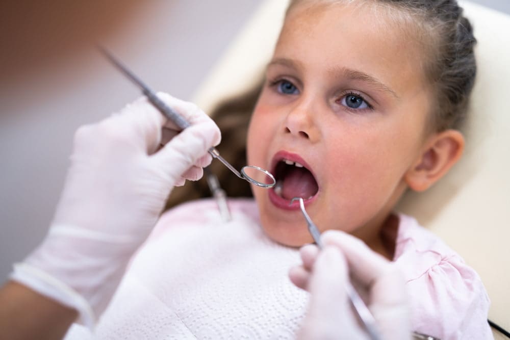 Young girl in a dental chair having her teeth examined by a dentist using a dental mirror and probe.