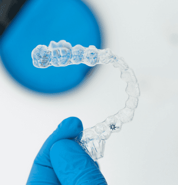 A gloved hand holding a clear orthodontic aligner, with a blue circular case in the background.