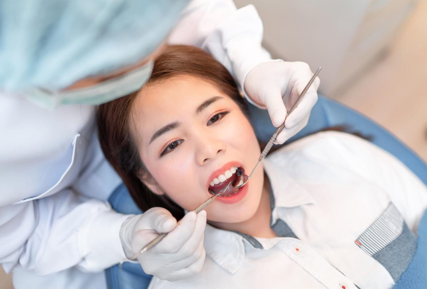 A woman is having a dental checkup at Best Orthodontics. A dentist holds a mirror and probe to examine her teeth as she lies comfortably in the dental chair.