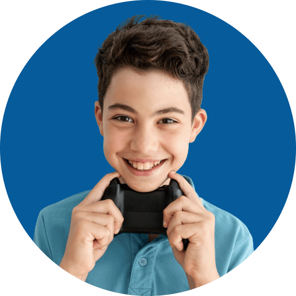 Boy in blue shirt smiling, holds a gaming controller against his chin, with a blue background.