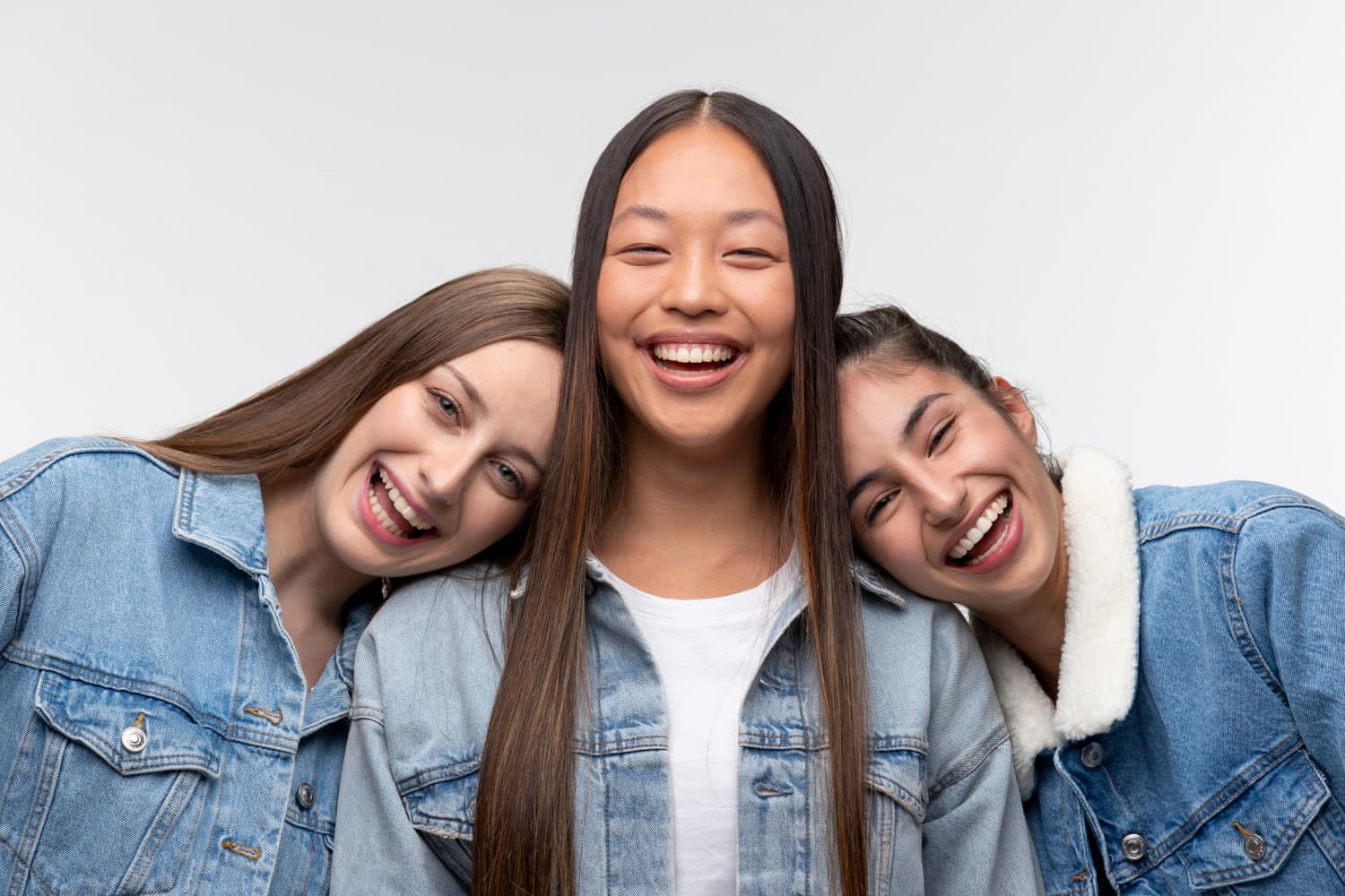 Three people, showcasing their best orthodontics with confident smiles, wear denim jackets as they pose against a plain background.