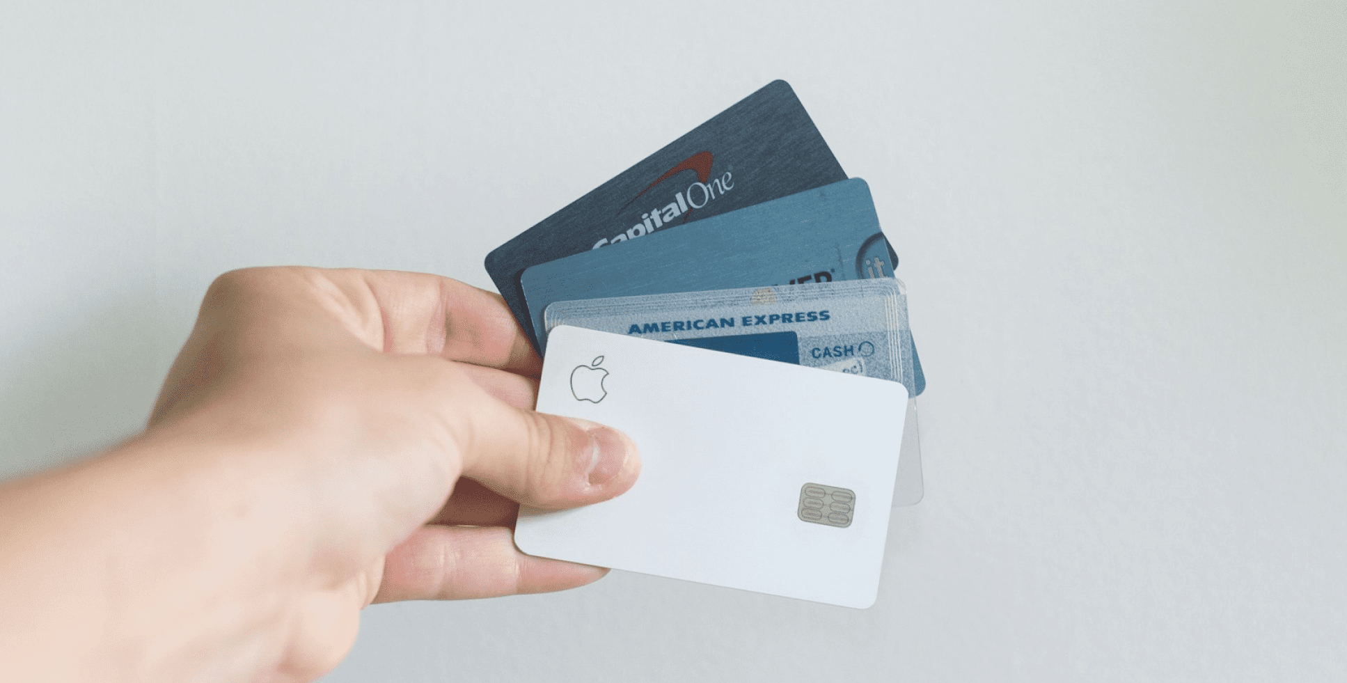 A hand holds several credit cards, including Apple Card, Capital One and American Express, fanned out.