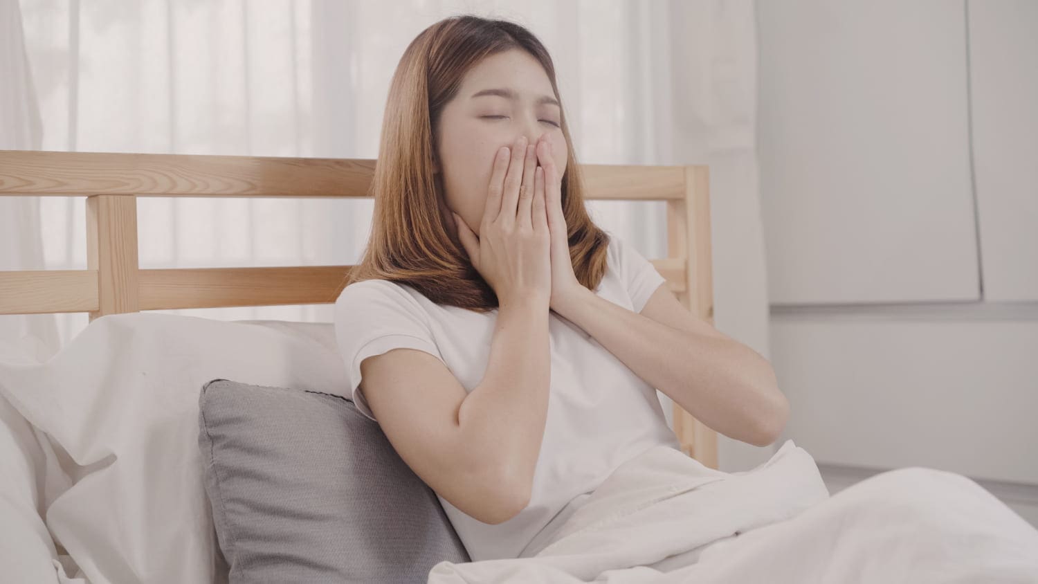 Woman sitting in bed yawning with her hands covering her mouth