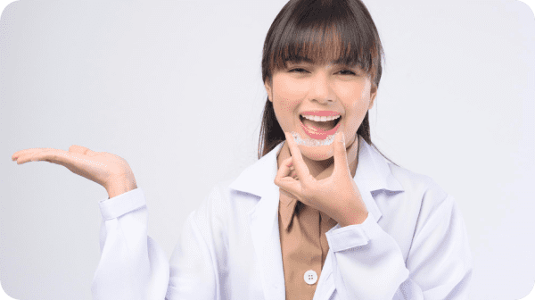 Person in a white coat smiling and holding a dental aligner.
