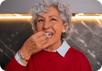 Elderly woman with curly gray hair in red sweater taking a pill.