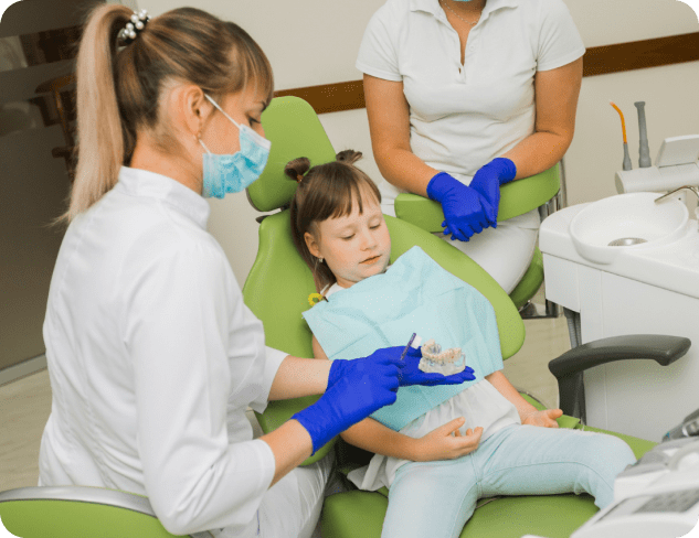 Dentist showing a dental mold to a child sitting in a dental chair while an assistant looks on.
