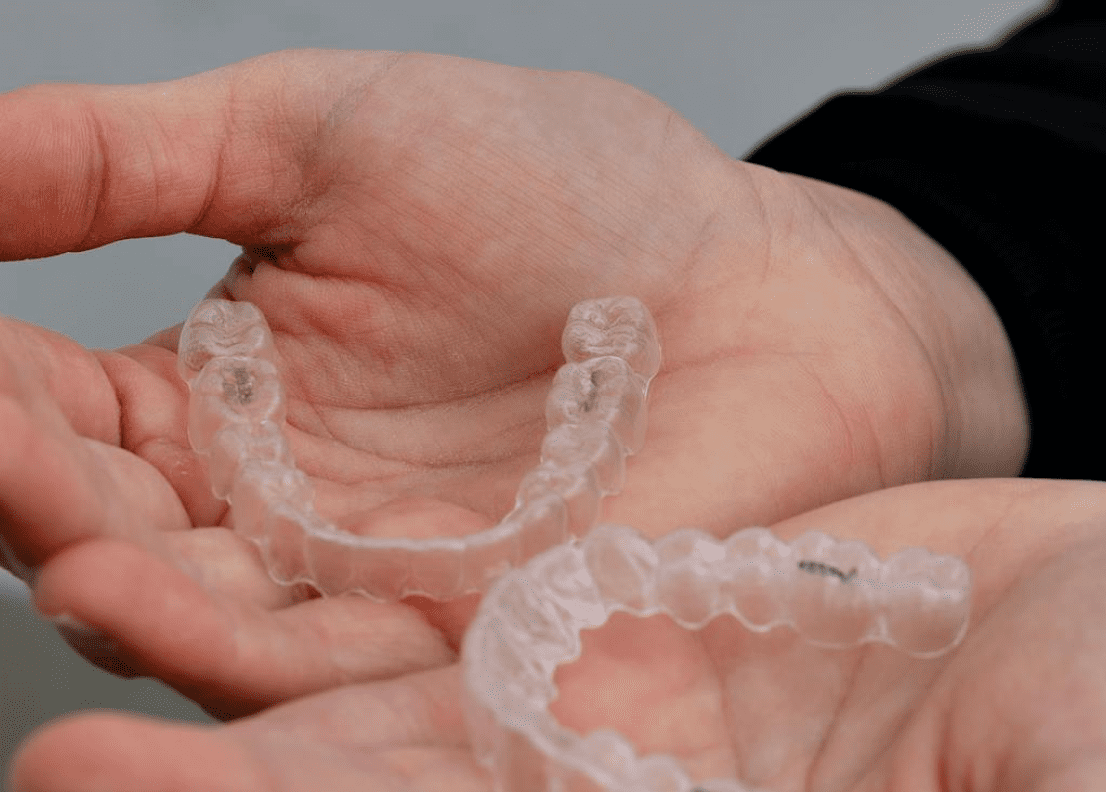 Hands holding two clear dental aligners.
