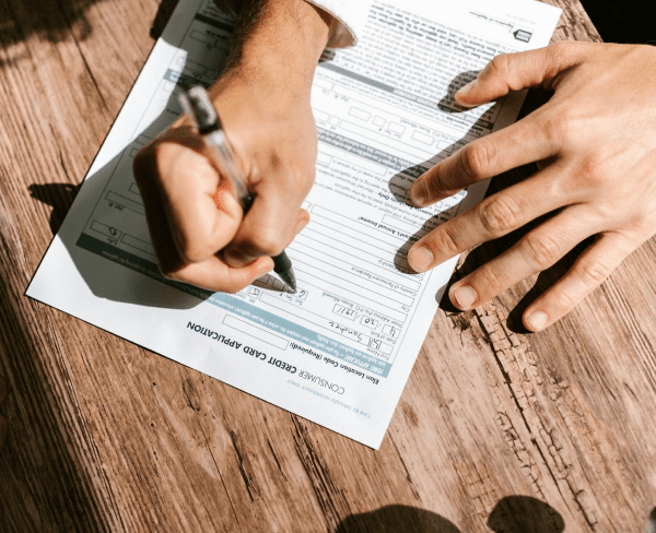A person fills out a commercial credit card application form on a wooden table.