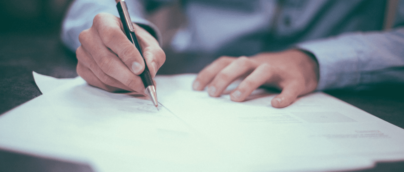 Person writing on a paper with a pen, wearing a long-sleeved shirt.